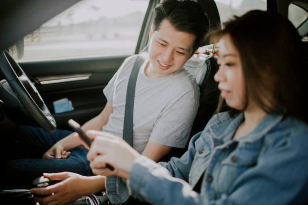 朝のロードトリップの前に道路側で電話gpsをチェックするアジアの中国の若いカップル - car map car rental land vehicle ストックフォトと画像