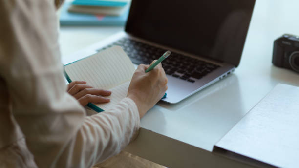 istock Female hand writing on schedule book while working with laptop on the table 1289300015