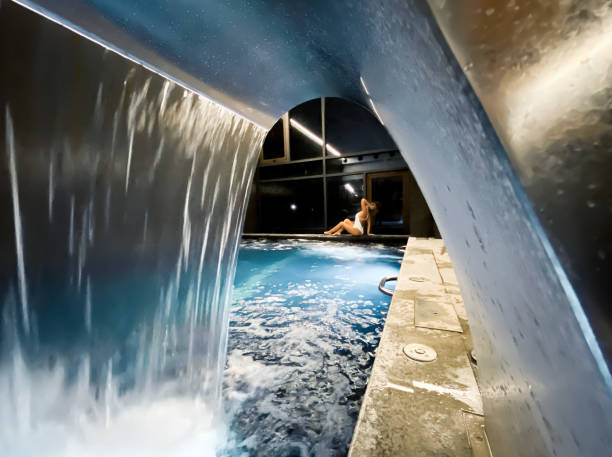 Beautiful woman photography view from waterfall spa with thermal water falling hands on head posing in a white swimsuit in a spa swimming pool blue colors at night view, Portugal photography - fotografia de stock