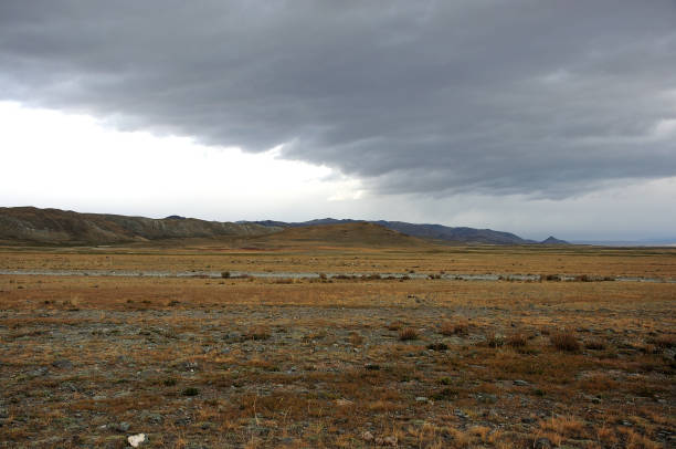 Dense thunderclouds over the autumn steppe and mountain ridges. Chuya steppe, Altai, Siberia, Russia.
