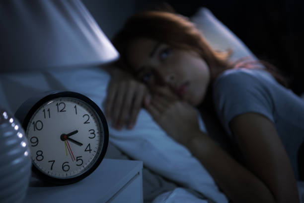 istock A depressed young woman lying in bed cannot sleep from insomnia. Selective focus on an alarm clock 1289303635