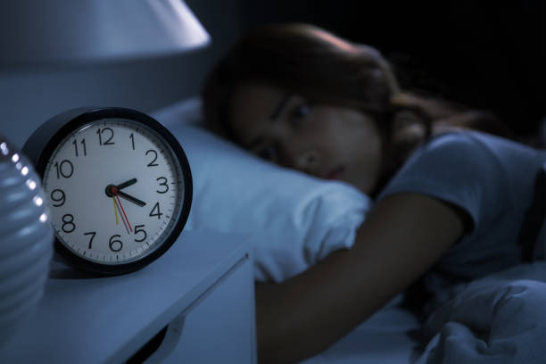 istock A depressed young woman lying in bed cannot sleep from insomnia. Selective focus on an alarm clock 1289303646