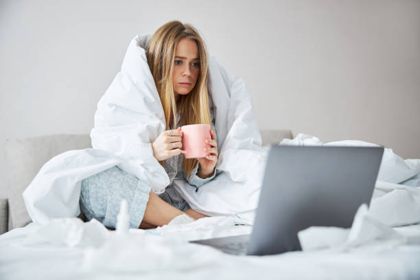 istock Young woman with flu drinking tea and using notebook at home 1289306913