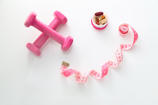 Pink dumbbell, supplements and tape measure on white background