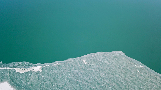 The boundary between the ice and the lake. The view from the top. Green water and white ice. Big lake Balkhash in Kazakhstan. Early spring. Ice breaks are visible, and white snow lies in places.