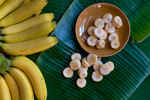 Fresh bananas are peeled and cut into pieces, put on a brown dish, placed on a green banana leaf background.