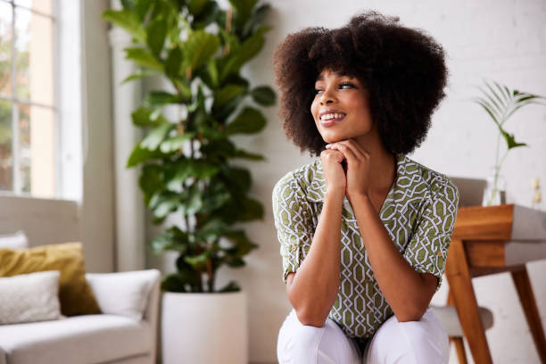 istock Smiling young woman sitting on a stool lost in thought and smiling 1289317434