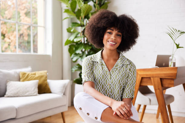 istock Young woman smiling while sitting on stool in her living room 1289317493
