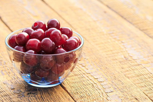 Fresh cherries in glass bowl on old wooden surface. Sweet ripe cherries in glass bowl on rustic wooden boards with copy space.