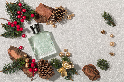 Perfume sprayer with christmas balls, fir tree branches and christmas ornament on silver background