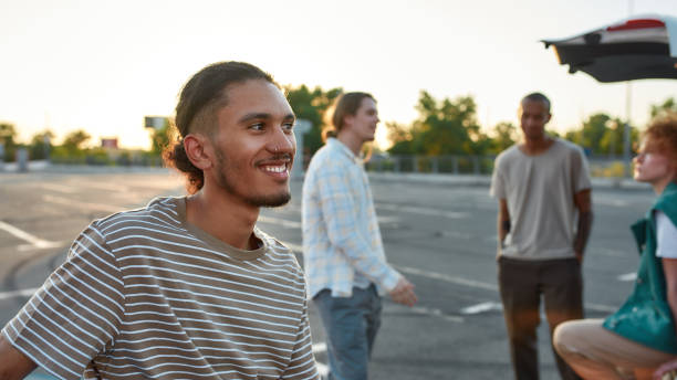 istock A close up of a casually dressed dark-skinned latina guy with a piercing smiling standing outside on a parking site with his friends on a background 1289326171