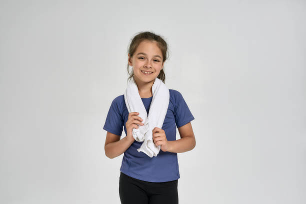 little sportive girl child in sportswear smiling at camera, holding towel around her neck while standing isolated over white background - gymnastics smiling little girls only isolated on white imagens e fotografias de stock