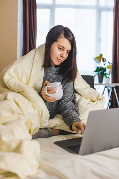 istock woman working on laptop in bed and drinking coffee 1289328371