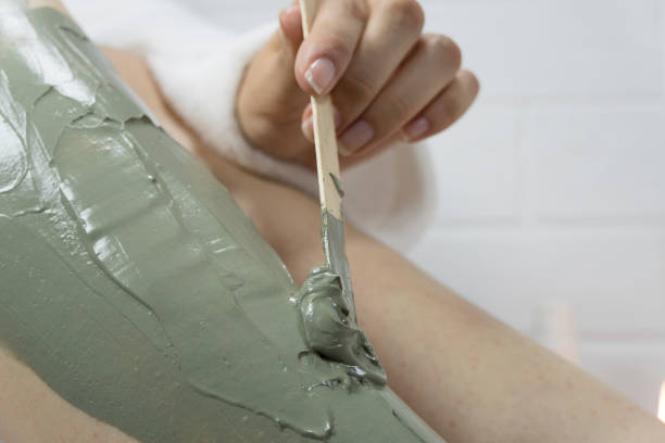 A woman applies a clay mask with a spatula to the skin of her legs. Irritation after depilation, shaving. Home skin care, body. SPA, moisturizing, treatment. Exfoliation, peeling. Strawberry legs. una mujer aplica una máscara de arcilla con una espátula en la piel de sus piernas. irritación después de la depilación, afeitado. cuidado de la piel en el hogar, cuerpo. spa, hidratante, tratamiento. exfoliación, pelado. patas de fresa.