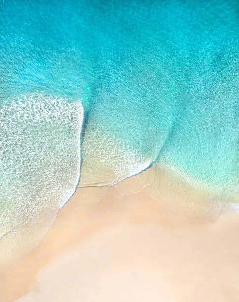 Photo of Aerial view of nice gentle waves crashing on an idyllic beach. Illustration of a travel paradise with beautiful blue turquoise water near a holiday destinations.