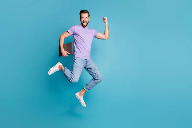 Full length body size photo of jumping high businessman with computer gesturing like winner smiling isolated on vivid blue color background.
