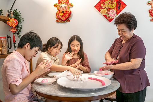 Young Asian Chinese boy and girl enjoying making glutinous rice dumplings (Tang Yuan 湯圓) with senior grandmother in preparation for Chinese New Year reunion dinner celebration