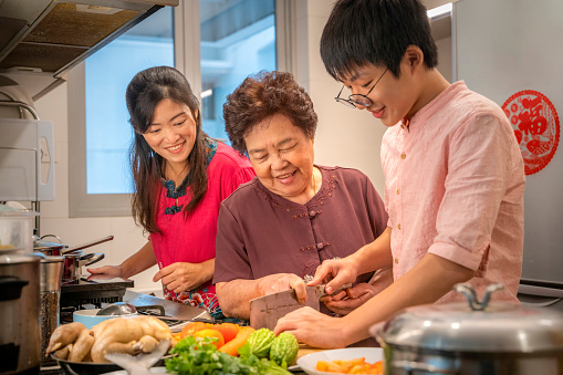 A bonding moment of young adult teen learning how to prepare vegetable for cooking from grand parent and mum.