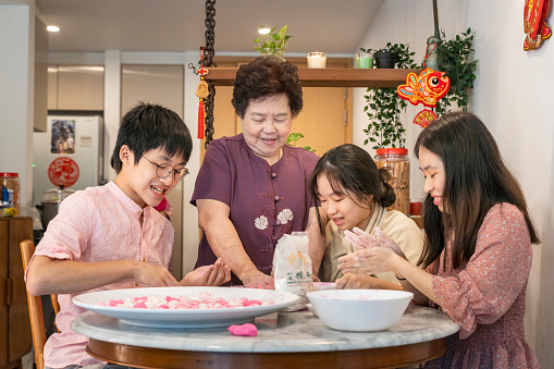Young Asian Chinese boy and girl enjoying making glutinous rice dumplings (Tang Yuan 湯圓) with senior grandmother in preparation for Chinese New Year reunion dinner celebration