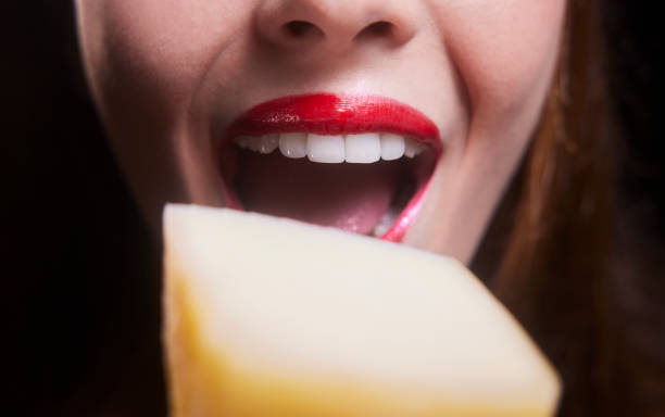 Close-up of young woman mouth biting piece of cheese