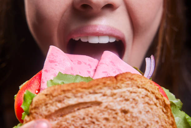 Close-up of young woman holding and eating letuce tomato onion ham sandwich