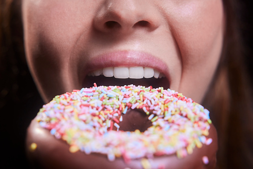 Close-up of young woman mouth eating colorful sprinkled donut