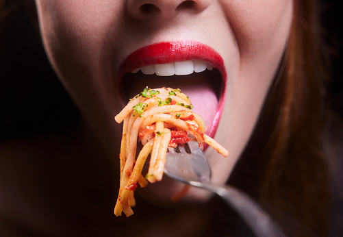 Close-up of a young woman mouth eating spaghetti pasta bolognese on a silver fork