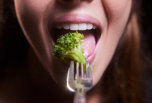 Close-up of young woman mouth eating broccoli on a silver fork