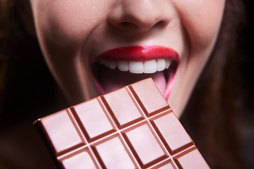 Close-up of young woman mouth biting chocolate bar