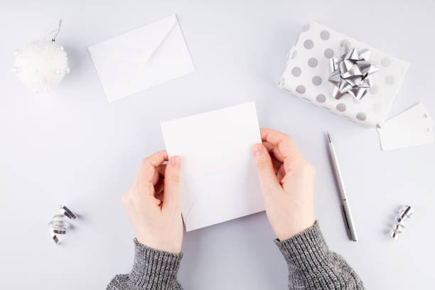 istock Woman puts card in white envelope for gift in silver packaging, gray background. Concept of preparation for holidays 1289349793