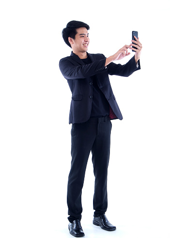 Portrait of young man taking a selfie with his smartphone while standing over white background