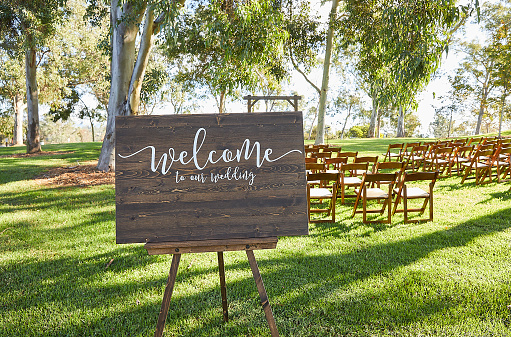 Welcome to our Wedding Wood Sign in front of outdoor event chairs on grass