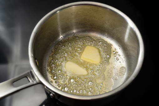 Melting butter in a stainless steel saucepan on the black stove, cooking concept, selected focus, narrow depth of field