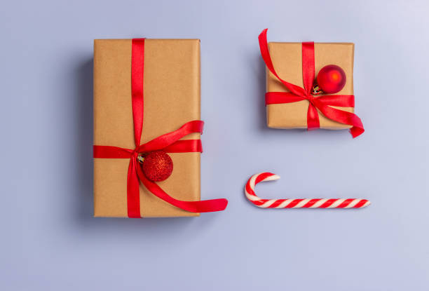 istock Gift boxes wrapped with paper kraft, red ribbon  and balls, candy on sticks on a light background. Top view. Presents for the holiday, Christmas. 1289358358