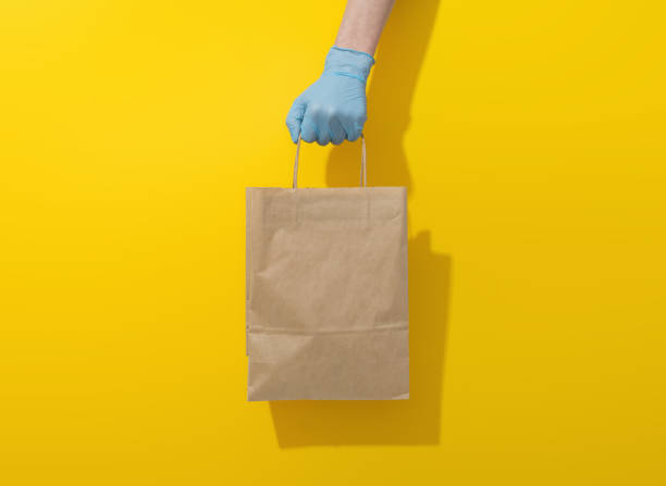 istock Hand in a blue glove holds a paper package on a yellow background 1289361691