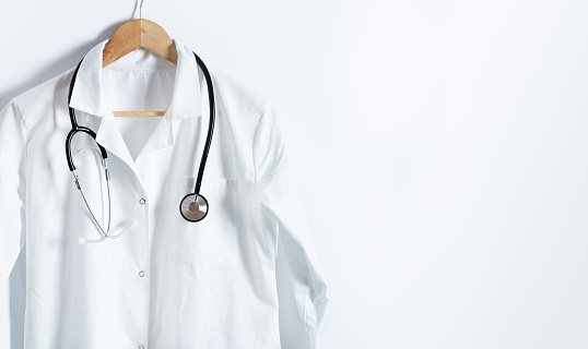 La capa blanca del doctor con estetoscopio en la percha sobre el fondo blanco con espacio de copia. photo