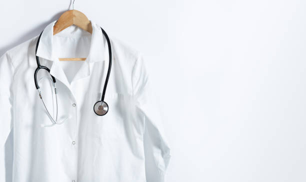 manteau blanc du docteur avec le stéthoscope sur le cintre au-dessus du fond blanc avec l’espace de copie. - blouse de laborantin photos et images de collection