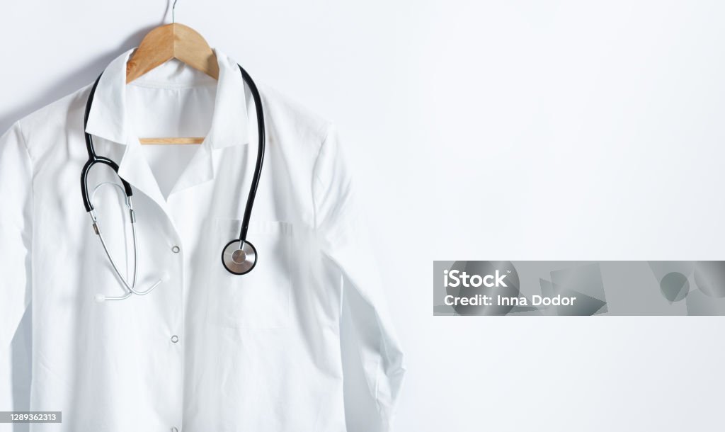 Doctor's white coat with stethoscope on hanger over white background with copy space. Doctor's white coat with stethoscope on hanger over white background with copy space. Healthcare and medical concept. Lab Coat Stock Photo