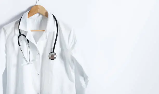 Doctor's white coat with stethoscope on hanger over white background with copy space. Healthcare and medical concept.