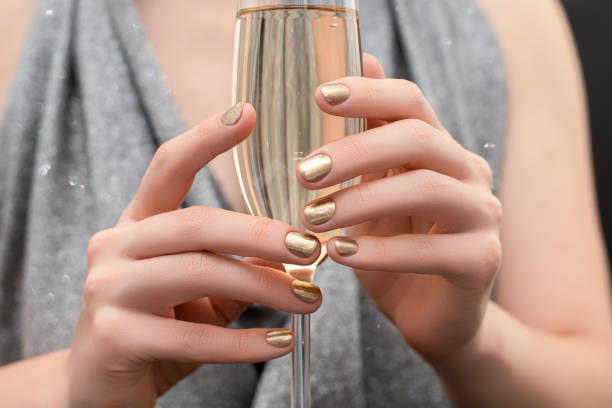 Female hands with gold nail design. Gold glitter nail polish manicure. Woman hold champagne glass