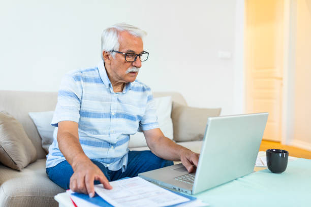istock Focused grey-haired elderly man sit on couch reading bank notifications calculating domestic expenditures, concentrated modern mature male consider financial paperwork, pay bills on laptop online 1289364122