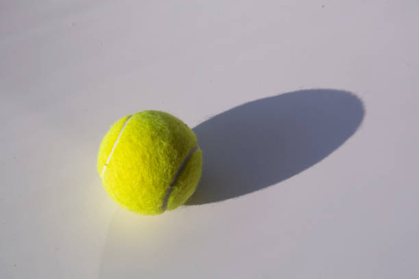 White tennis racquet resting on three tennis balls on a blue court lying in the corner surrounded by two white lines in the corner of the court.