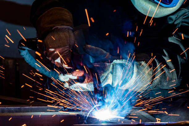 istock Employee welding steel with sparks using mig mag welder - focus on sparks. 1289369518