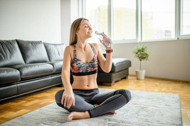 istock Sporty woman drinking water after intensive training at home 1289369744
