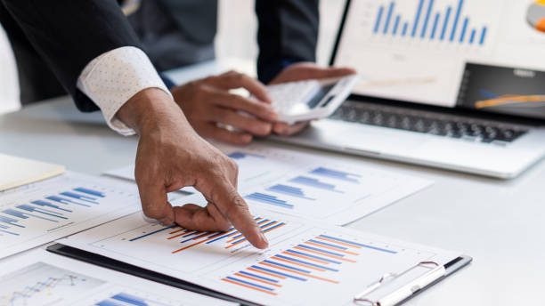 istock Male hand pointing to business graph document during conference room conversation. Laptop background. 1289371383
