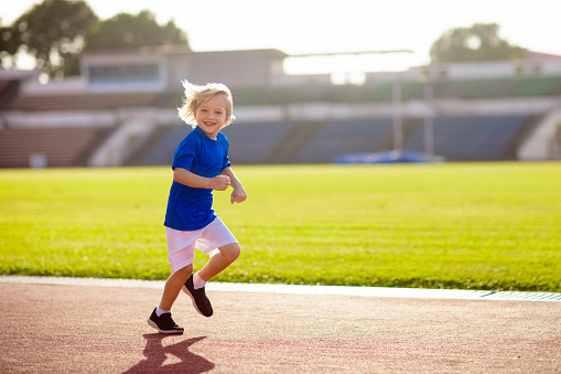 Child running in stadium. Kids run on outdoor track. Healthy sport activity for children. Little boy at athletics competition race. Young athlete in training. Runner exercising. Jogging for kid.