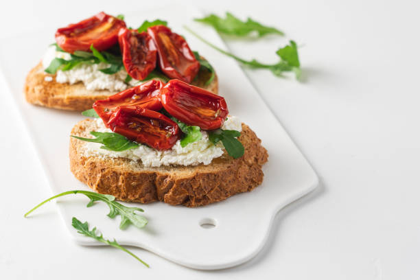 Bruschetta with sun dried tomatoes and arugula. Delicious breakfast or wine snack. White background, close-up view