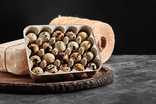 Quail eggs in a gray cardboard box. Close-up photo. Black concrete background. Healthy protein foods. Small speckled eggs for breakfast.