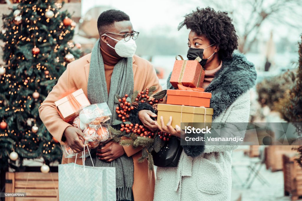 Young couple at Christmas shopping, COVID-19 pandemic. They wearing a protective mask to protect from corona virus COVID-19 Young couple at Christmas shopping, COVID-19 pandemic. They wearing a protective mask to protect from corona virus COVID-19 and holding gift boxes Christmas Stock Photo