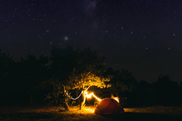 Magic night outdoors- setting camping in the forest with tent, a car and the lights, under the star sky